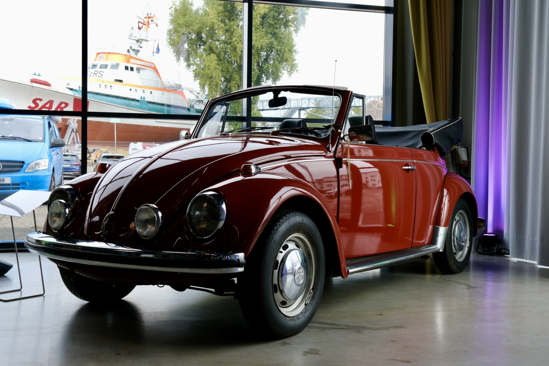 Klassischer roter VW Käfer Cabrio als Ausstellungsstück im Hangar 10 mit Blick auf weitere historische Fahrzeuge und Schiffe